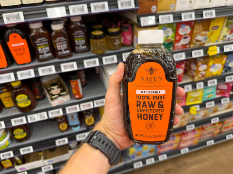 Nate's Raw Unfiltered Honey Bottle Held In Grocery Aisle
