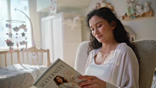 Pregnant woman relaxing nursery armchair reading magazine. Belly closeup.