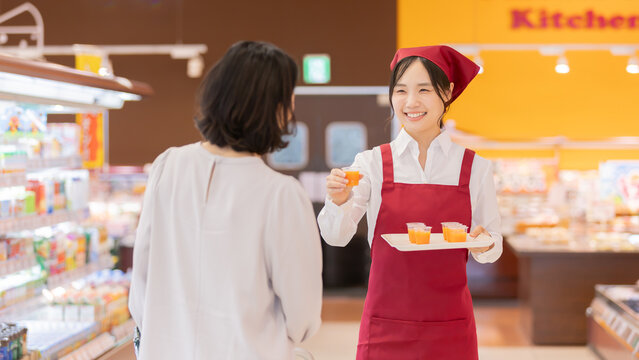 スーパーマーケットで女性客に試飲ドリンクを勧める笑顔の女性スタッフ