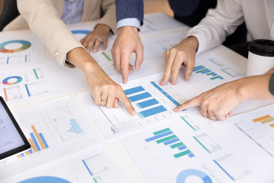Diverse professional marketing strategists or startup founders team working with analytics reports and statistical data interacting with paper and digital tools analyzing and making decision. Close up