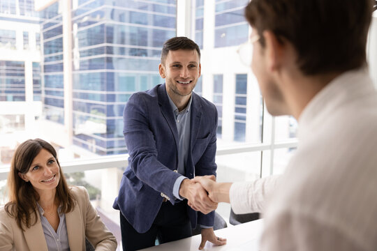 Friendly hr manager working in team with female partner greeting professional candidate with handshake after successful hiring interview welcoming new employee to company starting onboarding process