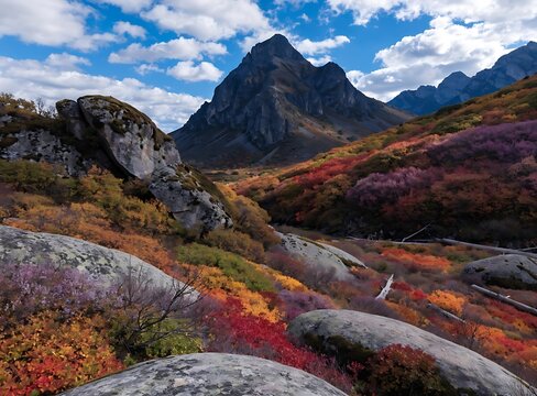 Rugged mountain landscape with rocky slopes and autumn foliage under a blue sky with clouds