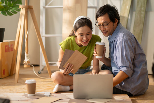 Asian couple of home owners discussing new renovate home,wood samples,moving box,interior design improvement,new design for new home.asian chooses a sample floor for his new apartment