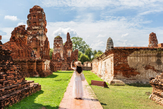 Young female tourist in a white dress walking through the ancient brick ruins of Wat Mahathat in Ayutthaya Historical Park, Thailand