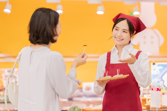 スーパーマーケットで女性客に試食を勧める笑顔の女性スタッフ
