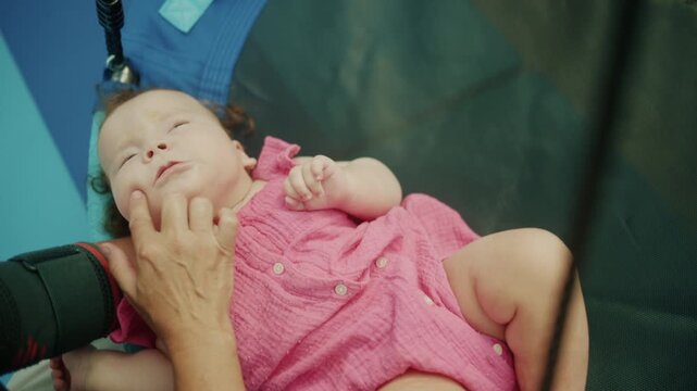 Baby girl lying down in a pink dress, receiving a gentle facial massage from an adult hand, focusing on care and rehabilitation