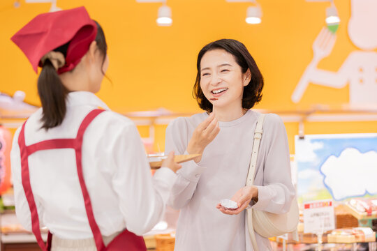 スーパーマーケットで試食を楽しむ笑顔の女性客と接客する女性スタッフ