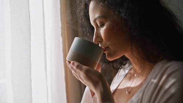Expecting mom drinking coffee window. Close up hand caressing pregnant belly.