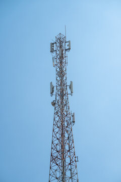 Lattice type telecommunications tower, also known as a base transceiver station (BTS). Panel antennas and remote radio units are mounted on its steel framework against a backdrop of a clear blue sky.