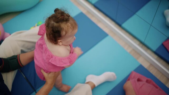 Baby girl discovering her reflection in a playroom mirror, supported by an adult. Developing self awareness in a safe environment