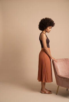 Stylish black woman posing next to pink chair in elegant fashion