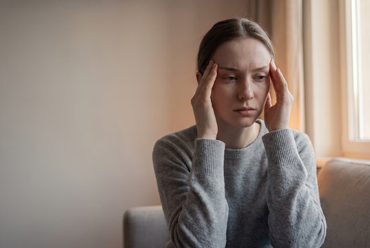 Tired woman holding head with stressed expression in warm interior