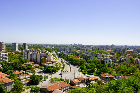 Aerial view of a city with apartment buildings, houses, and a busy road with cars on a clear day.