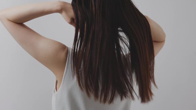 後ろ姿で長い髪を手ぐしで整える女性