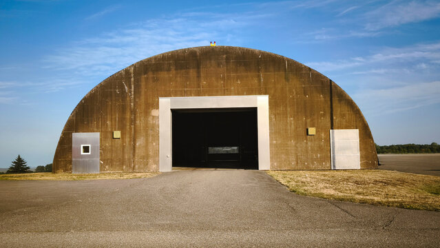 Hardened aircraft shelter on a military airfield. Weathered concrete bunker with open hangar doors. Cold war era military infrastructure and aviation storage