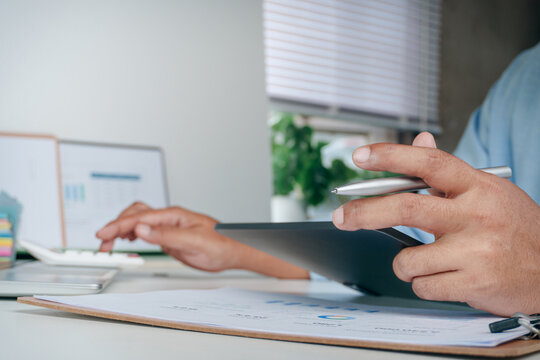 Business professional holding digital tablet and stylus pen while using calculator for financial calculation on office desk, concept of mobile business technology, accounting,