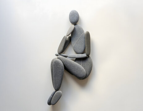 Abstract stone figure, minimalist human sculpture, contemplative pose, smooth gray pebbles arranged on a clean white background, representing thought, stillness