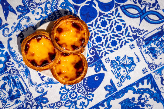 Three pastel de nata custard tarts overhead on blue and white