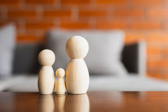 Family life insurance and healthcare planning concept with wooden peg doll figures of parents and child standing on table with warm brick bokeh background for protection and investment.