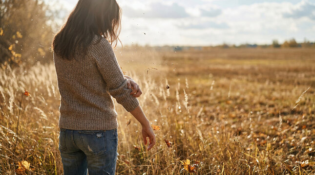 Young woman scratching her arm due to seasonal allergy symptoms while standing in a dry golden grass field during autumn sunset experiencing skin irritation and pollen sensitivity outdoor.