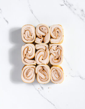 Lean turkey slices rolled tightly and arranged in a repeating geometric pattern on a white marble background.