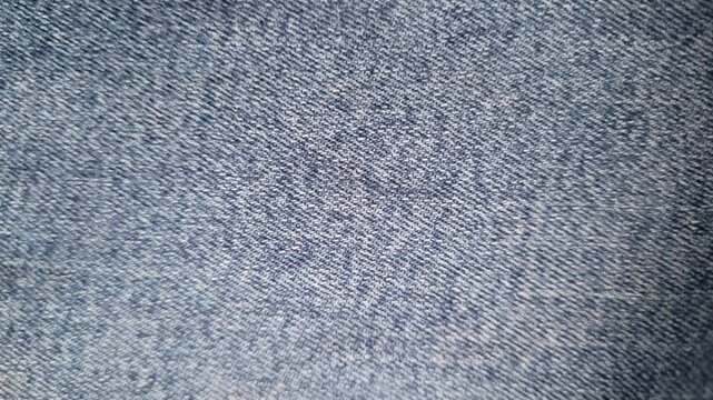 Detailed macro texture of washed blue denim fabric with woven stone cotton fiber pattern and soft natural lighting 4k video