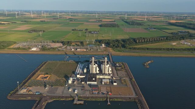 Aerial view of a combined cycle gas turbine power station providing electricity, with a large wind farm and substation in the background
