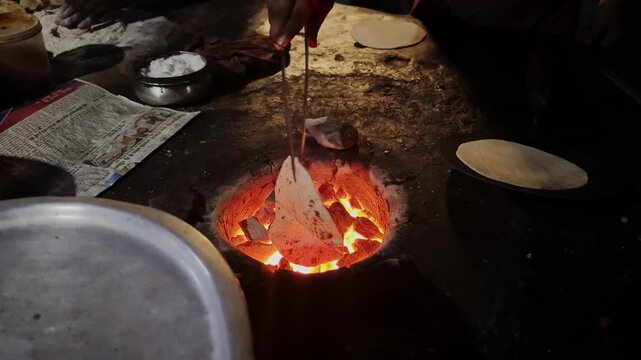 Traditional Indian roti being cooked directly over a hot wood fire at a rustic roadside food stall