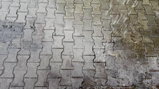 Water falling from a roof onto wet interlocking brick pavement creating ripples and splashes during heavy monsoon weather