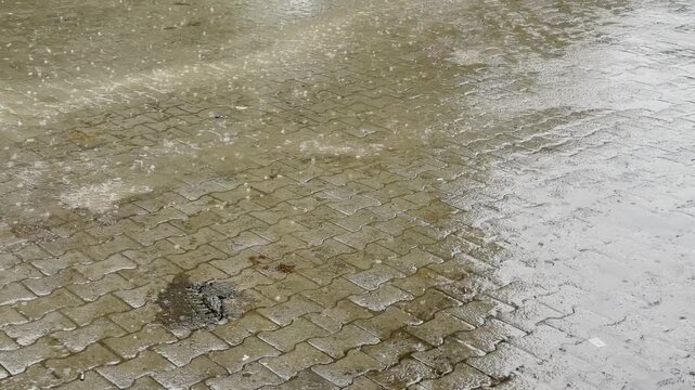 Close up of raindrops hitting shallow puddles across wet interlocking brick pavement during a heavy monsoon shower