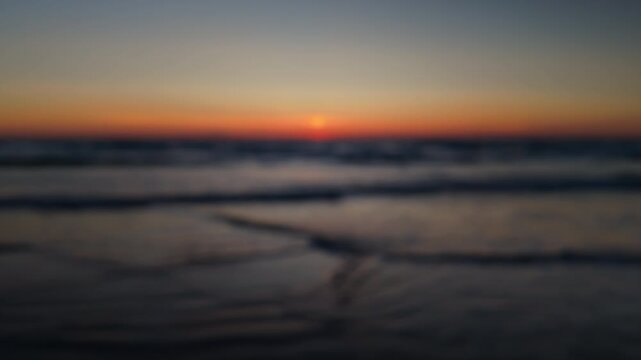 Soft blurry sunset over the ocean with gentle waves and a calm beach shoreline, creating a peaceful evening background with warm colors and a dreamy mood