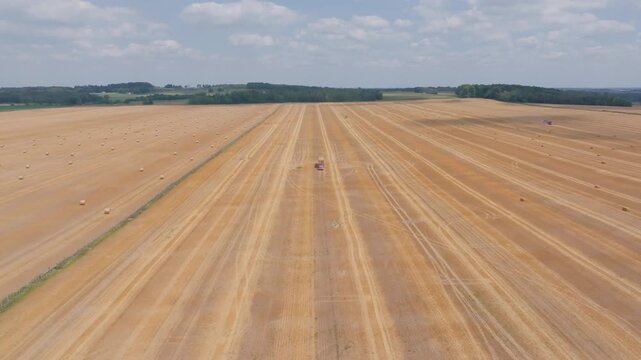 A red tractor pulls a baler through a golden harvest field in Bruce County, Ontario. Scattered round straw bales dot the expansive rural landscape under a bright summer sky.