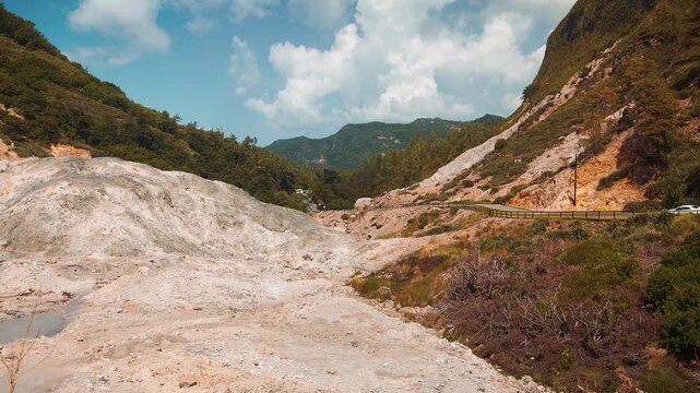 Scenic view of the Soufri&egrave;re Drive-In Volcano in Saint Lucia, showcasing pale sulphuric rock formations, lush green mountains, and the winding path through the geothermal landscape.