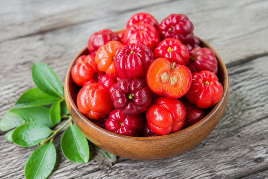 Fresh acerola cherries in wooden bowl with leaves on grey table, healthy fruit and natural food concept
