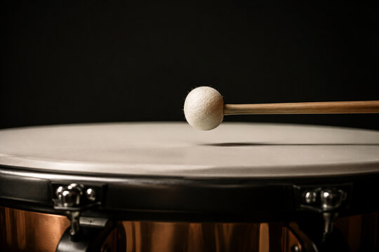 Drumstick poised just above the skin of a timpani drum.