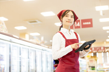 Fototapeta premium スーパーの冷蔵売り場でタブレットを使い商品管理をする女性店員