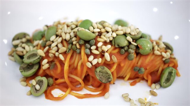 Fresh spaghetti pasta with tomato sauce garnished with pine nuts and olives on a white ceramic plate.