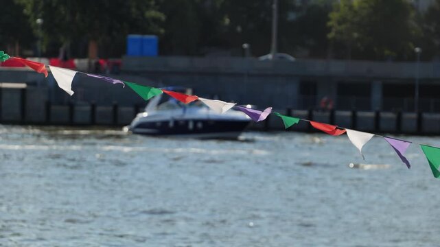 Colorful pennant flags waving over river water with blurred boat and city background