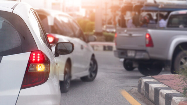 Rear side of white car with turn on right signal waiting to make a U-turn. Cars are stopped in a heavy traffic queue on a city street during a busy daytime commute with bright sunlight.