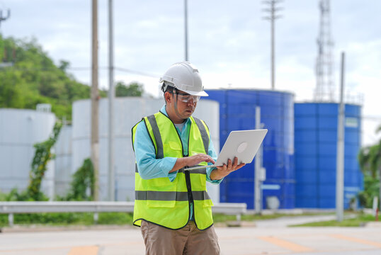 Industrial engineer hard hat safety vest laptop water tank utility plant worker inspection maintenance outdoor male technician at blue facility site
