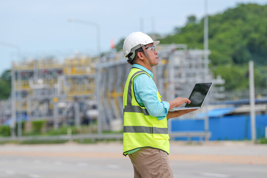 Engineer construction hard hat safety vest laptop site male worker uses computer at outdoor industrial project with road scaffold green hill focused expression