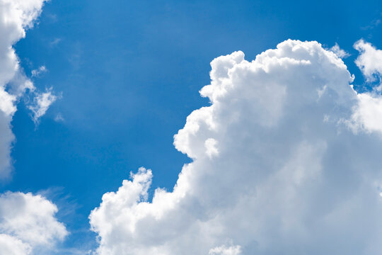 Towering white cumulus cloud rising into deep blue summer sky