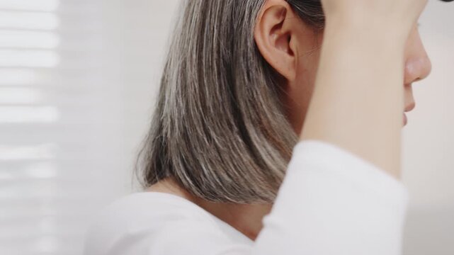 Close-up shot Asian mature woman with natural grey hair gently brushes her short hair.