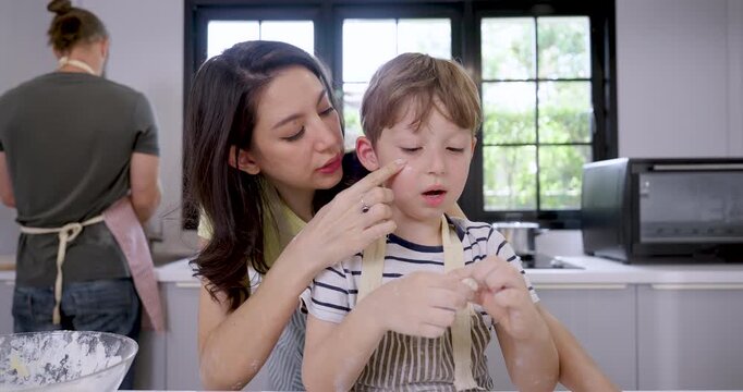 Slow motion Caucasian mother playfully dabs flour on young son's cheek while boy shapes dough by hand, creating joyful home baking lesson with nurturing parenting and warm family connection.