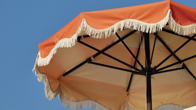 Orange retro beach umbrella with fringe providing shade on a sunny day