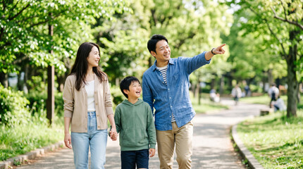 Fototapeta premium 新緑の公園を笑顔で散歩しながら遠くを指差す仲良し家族