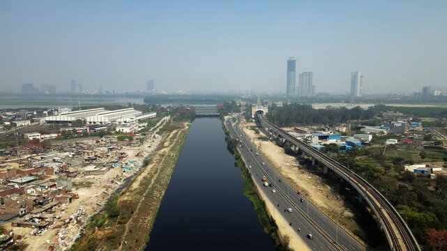 Aerial view of traffic timelapse in Delhi city featuring busy roads alongside a metro track running parallel to a river.