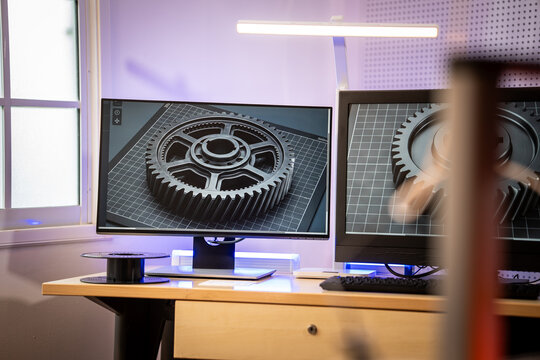 Dual computer monitors in a modern office showing a 3d gear model on a design workspace