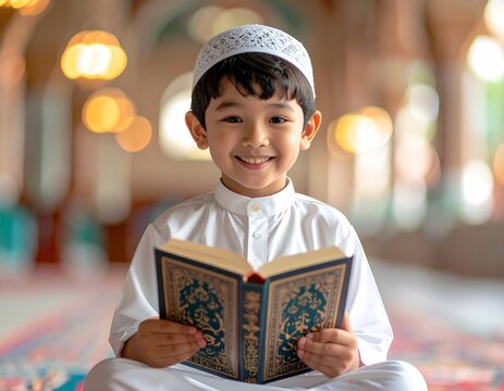 Young boy in traditional attire reading Quran inside mosque with warm lighting.