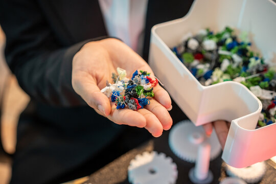 Close up of a hand holding small colorful recycled plastic pieces beside a sorting machine, showing recycling, waste reduction and sustainable manufacturing